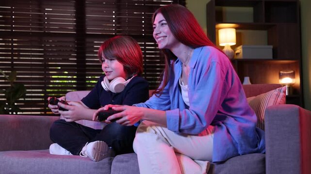 Emotional mother and son with controllers playing video game on sofa at home