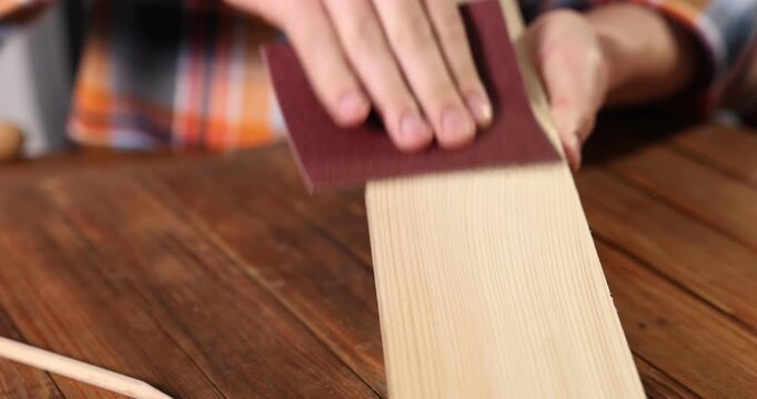 Man polishing wooden plank with sandpaper at table, closeup