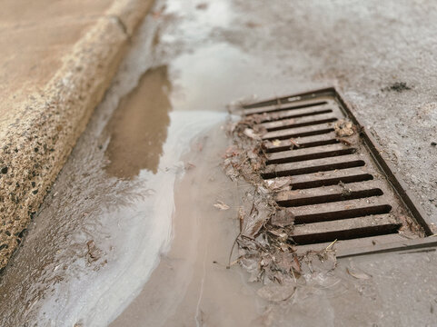 Une plaque d'&eacute;gout au milieu de la route, d'o&ugrave; s'&eacute;coule de l'eau. Mise au point s&eacute;lective.	