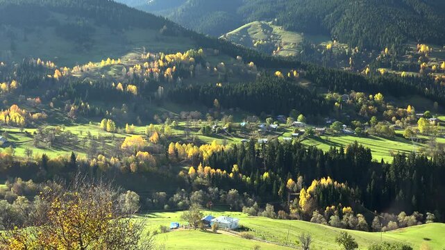 Alps village in mountain valley with autumn forest, green meadows, panoramic cinematic landscape. Scenic hamlet among fall woods and rolling highlands, fairy tale countryside vista, vivid.