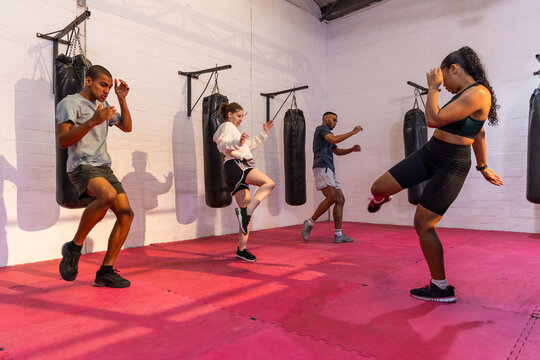 Diverse classmates with teenager practicing kickboxing at boxing studio on pink mats with bags