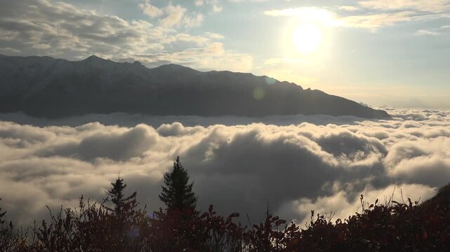 Alps mountain peaks rise above cloud sea as sunrays pierce mist, cinematic landscape view. Swiss range summits overlook overcast layer, god rays through vapor, breathtaking highland vista.