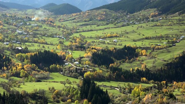 Alps village in mountain valley with autumn forest, green meadows, panoramic cinematic landscape. Scenic hamlet among fall woods and rolling highlands, fairy tale countryside vista, vivid.