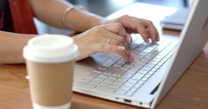 Woman typing on laptop after brief pause, working on document with coffee cup nearby
