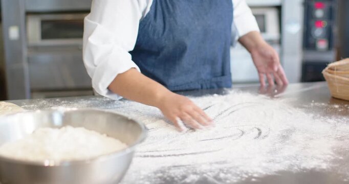 African American woman in chef jacket scooping flour from mixing bowl, dusting prep table for dough