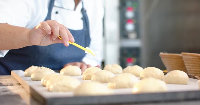 Female pastry chef reaching, brushing dough rows with yellow brush at bakery for baking, copy space