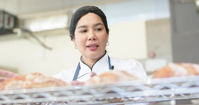 Vertical video: Bakery chef scanning rack then touching loaves, adjusting spacing for even cooling