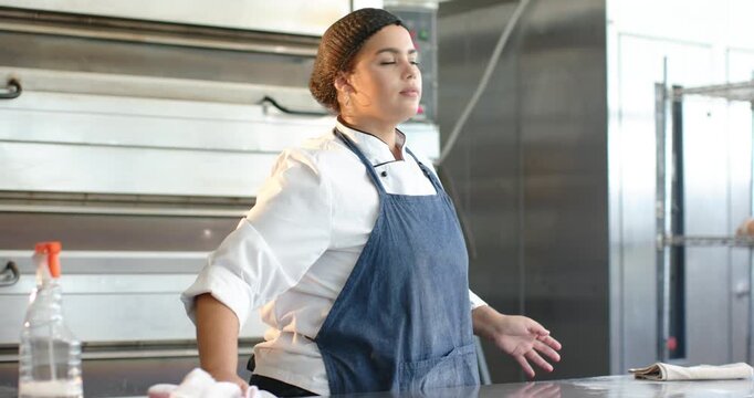Mid adult chef in jacket checking oven controls, wiping counter with pink cloth prepping in kitchen