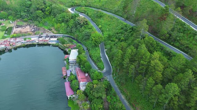 Aerial drone footage of a beautiful winding road near Lake Toba, North Sumatra, Indonesia, surrounded by green hills and stunning natural landscape.