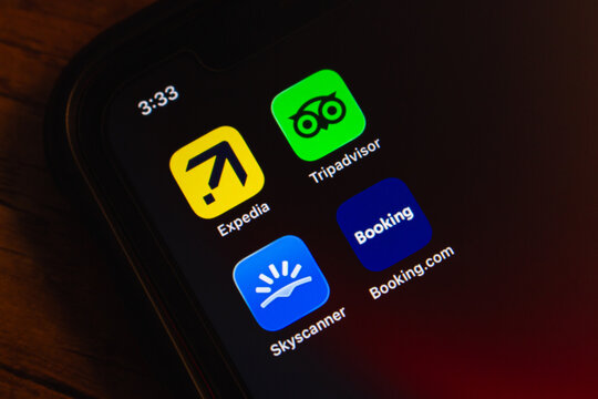Mexico City, MEXICO - Mar 19 2026 : Close-up of an iPhone screen showing four major OTA app icons, including Expedia, Tripadvisor, Skyscanner, and Booking.com, on a dark wooden surface.