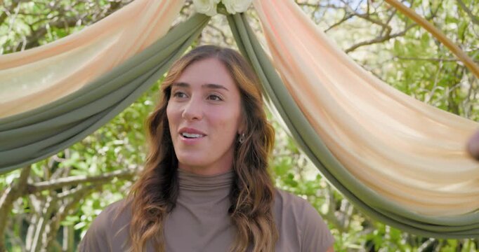 Woman officiant with tablet under arch in garden, camera pulling back revealing two men saying vows