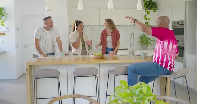 Diverse friends standing, sitting at wooden island, left man sharing news, group sipping mugs