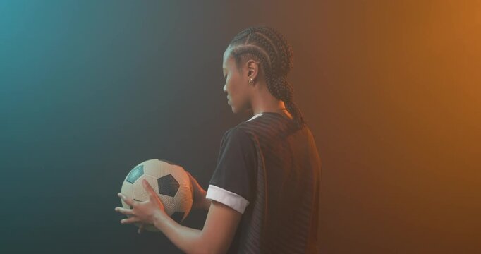 African American woman cradling soccer ball in dark jersey preparing for game in studio, copy space