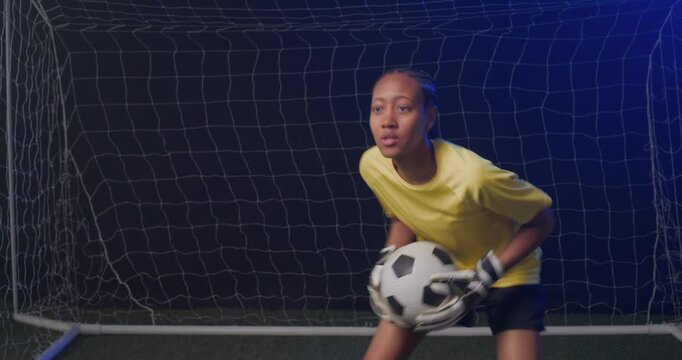 African American woman goalkeeper tracking shot, lunging and scooping ball at goal to prevent score