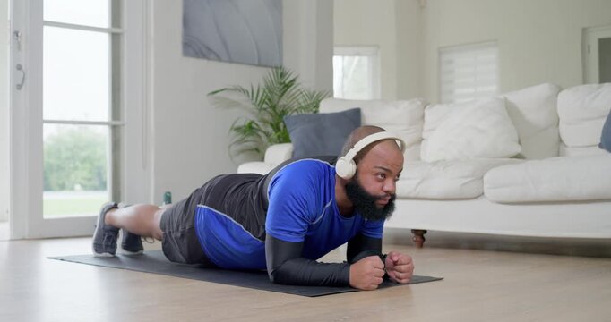 African American man in sportswear following audio doing plank kneeling on mat at home with headset