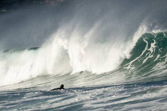 Massive crashing waves silohette surfer spray foam under dramatic cloudy skies