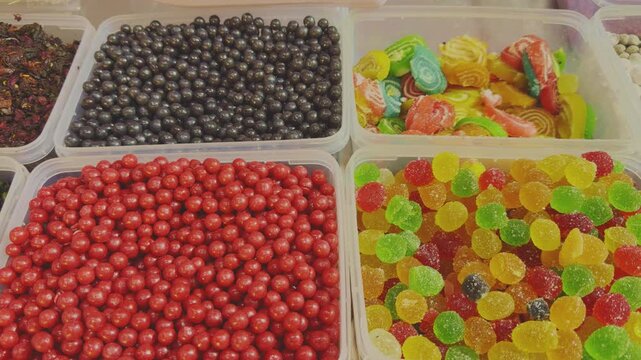 Tracking shot of assorted Indian mukhwas and churan candies in plastic containers, featuring vibrant sugar coated sweets in multiple colors and textures arranged in a neat display!
