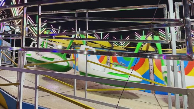 Static shot of a colorful break dance amusement ride at an Indian mela, featuring bright neon lights, moving seats, and vibrant patterns creating an energetic carnival atmosphere at night!