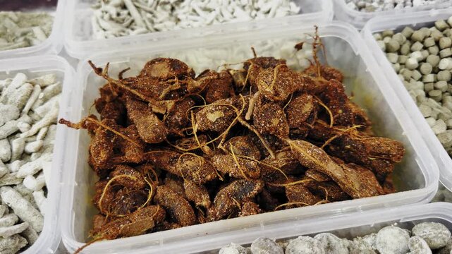 Closeup of peeled and sun-dried tamarind pods coated with spices, arranged in a container alongside other traditional items, showcasing rich texture and earthy tones in a local Indian market!