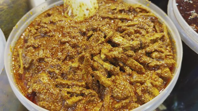Camera orbiting closeup of traditional Indian mango pickle, showing chunky raw mango pieces coated in rich spicy masala and oil with textured mustard seeds in a bowl!