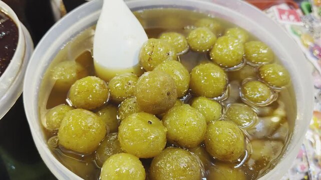 Camera orbiting closeup of amla murabba, showing whole gooseberries soaked in glossy sugar syrup with rich texture and natural shine in a traditional Indian sweet preserve!