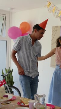 Woman raising arms and blowing horn couple dancing with horns near cake and balloons party planning