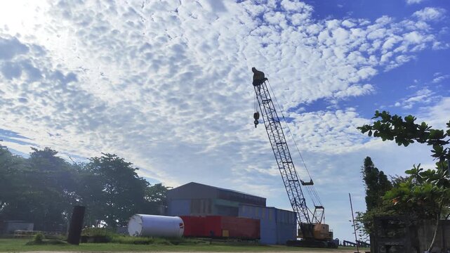 Time lapse footage of a crawler crane standing at an industrial site under a dramatic cirrocumulus cloudy sky with bright blue horizons.