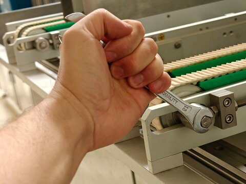 Male hand holding a wrench and loosening or tightening a tensioner bolt on a machine.