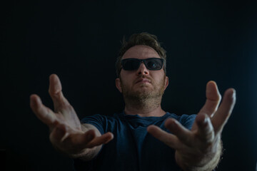 Naklejka premium Man wearing sunglasses reaching hands forward toward camera in dramatic pose