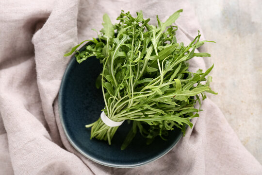Bowl with bunch of fresh arugula leaves on grey background