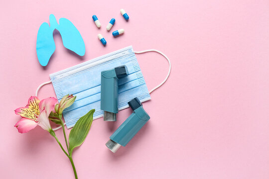 Asthma inhalers with medical mask, pills and alstroemeria flower on pink background