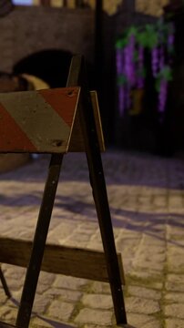 A construction sign is placed on a cobblestone street at night. The background shows some lighting with purple colors. The area appears quiet and empty with stone pavement.