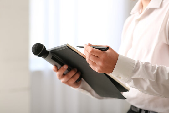 Male reporter with microphone and notebook in office, closeup