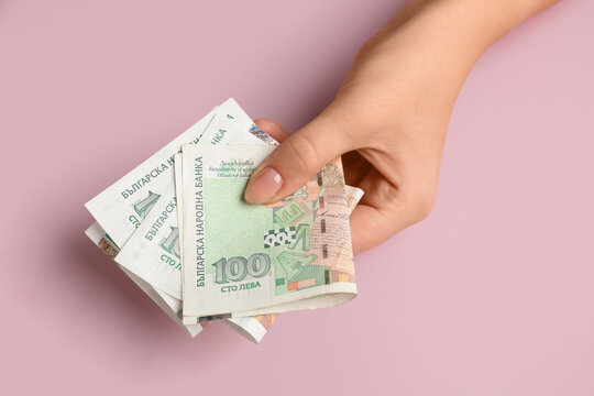 Female hand holding Bulgarian lev banknotes on pink background