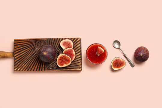 Glass bowl of sweet fig jam and wooden board with fresh fruits on pink background