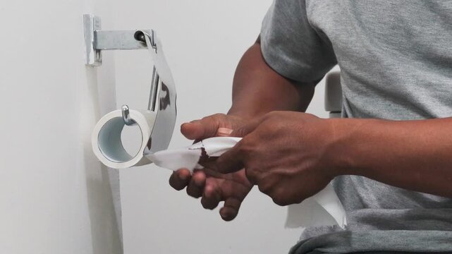 Close-up of Asian man hands unrolling toilet paper roll and tearing off a bit.