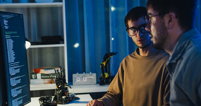 Team adult male engineer collaborate on robotic hand project using AI code solutions machine learning at tech workspace night. Artificial intelligence interface, collaboration prototype development.
