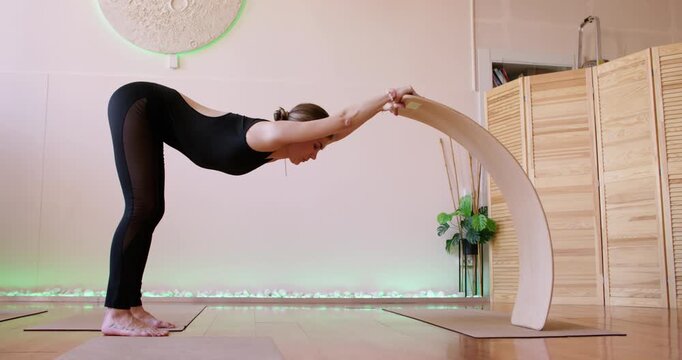 Healthy back. Fitness studio. Female exercising with wooden balance board as support bending forward for rehabilitation spine strength.