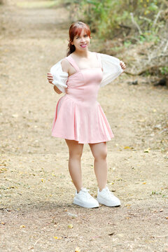 Mujer latina abriendo su chaqueta para mostrar el dise&ntilde;o de su vestido rosado, fotograf&iacute;a tomada al aire libre en un ambiente natural.