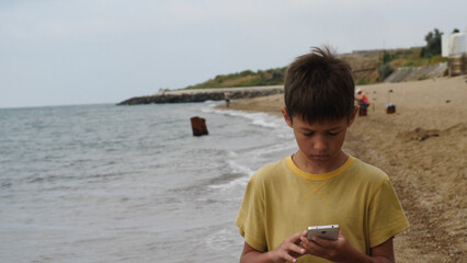 traveler boy walk on the beach and using smart phone in the evening, chats, write sms. Using a portable handheld device on summer vacation, internet. © vla