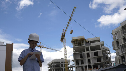 builder boy stands among builder cranes using tablet, boy plays a builder, have fun and enjoy © vla