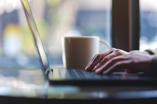 Closeup image of a woman working and typing on laptop computer in cafe