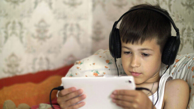 boy plays on the Tablet lying in the bed with headphones, have fun and enjoy