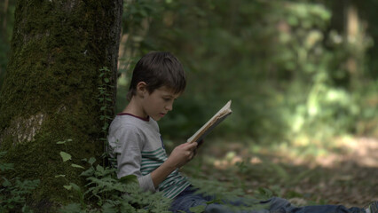 boy sits near a tree in the forest and reads a book, have fun and enjoy © vla