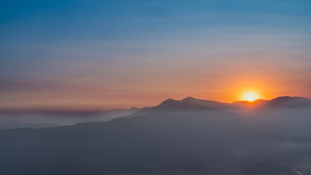 Dawn in the mountains. Early morning.  The sun is shining, rising over the ridge. The blue sky is highlighted with orange and pink. Fog, haze in the valley. Nepal. Pokhara. The Himalayas.