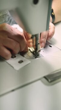 Vertical video. Seamstress sewing. Garment making. Seamstress hand preparing white eyelet tape with metal fittings. Fashion clothing studio workflow.