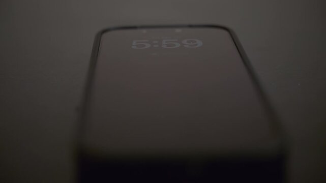 Smartphone alarm clock showing 6:00 on screen. Early morning wake up concept with mobile phone in dark room