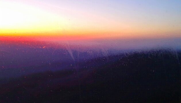 Spettacolare tramonto aereo con un orizzonte vibrante di sfumature arancioni, viola e blu, visto attraverso il finestrino di un aereo.