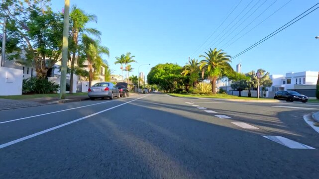 Dynamic first-person perspective driving through a sunny suburban street with green trees and residential homes.