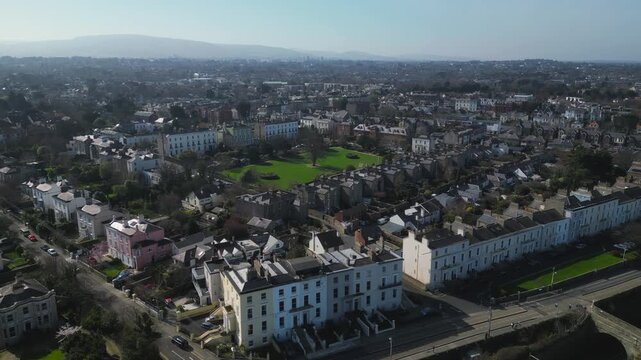 Aerial drone footage over Monkstown, Dublin, Ireland. Georgian architecture and leafy residential streets stretch toward distant mountains under clear winter sky.